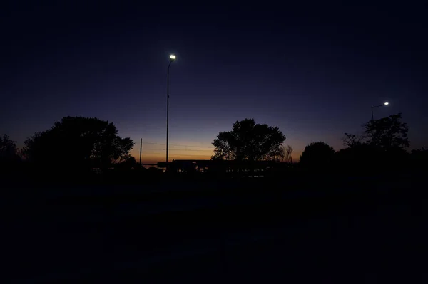夕暮れ時に車が通り過ぎる公園の隣の道 — ストック写真