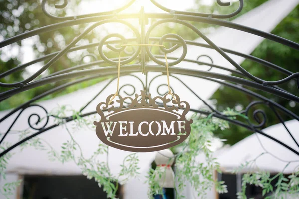 vintage welcome sign hanging on arched entrance in garden with sun light