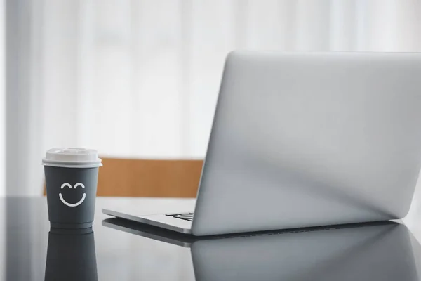 happy face icon on coffee paper cup with laptop on table, happy working concept