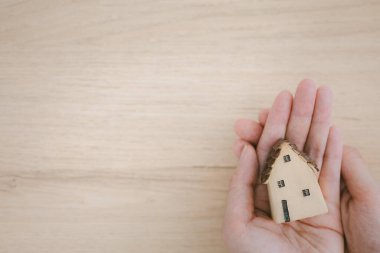 woman hands holding home model with care on wooden background, warm and care concept