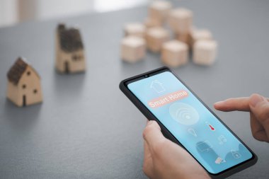 woman hand holding mobile phone showing smart home app screen with home model on background