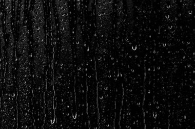 Temiz camın yüzeyinden aşağı siyah bir zemin üzerinde su damlaları akar. Yaratıcılık için doku.