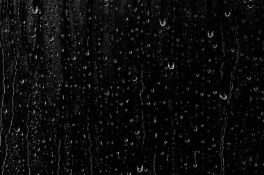 Temiz camın yüzeyinden aşağı siyah bir zemin üzerinde su damlaları akar. Yaratıcılık için doku.