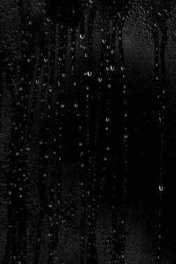 Temiz camın yüzeyinden aşağı siyah bir zemin üzerinde su damlaları akar. Çerçevenin dikey konumu. Yaratıcılık için doku.