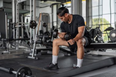 Asyalı adam spor yapıyor. Spor elbiseli genç bir adam spor salonunda silah egzersizi yapıyor..