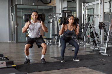 Asyalı kadın ve Asyalı erkek spor yapıyor. Spor salonunda birlikte çömelmiş egzersiz yapan sağlıklı bir çift..