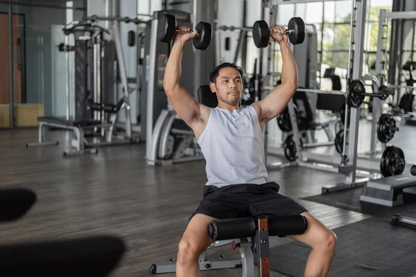 Asian man exercises in fitness. Young healthy man in sportwears doing shoulders exercise in gym.