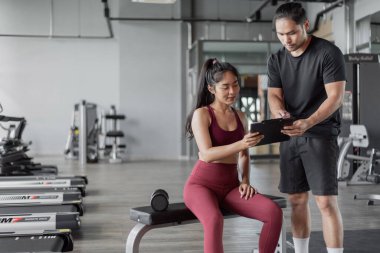 Spor salonunda kişisel antrenörle Asyalı kadın egzersizi. Kişisel antrenör sağlıklı bir kadınla egzersiz planı hakkında konuşuyor..
