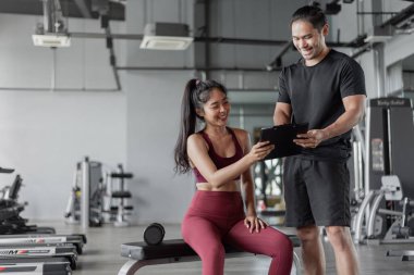 Spor salonunda kişisel antrenörle Asyalı kadın egzersizi. Kişisel antrenör sağlıklı bir kadınla egzersiz planı hakkında konuşuyor..