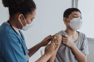Tıbbi maske takan Asyalı çocuk doktor tarafından aşı oluyor. Koronavirüsü önlemek için çocuk doktor ve hemşireden aşı oluyor. Bir klinikte Covid-19 aşı kampanyası.