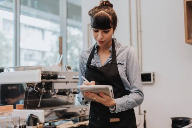 Kahve dükkanı tezgahının arkasında duran bir kahve sahibi. Kafede elinde dijital tabletle ayakta duran bir bayan barista. İş sahibi kavramı.