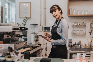 Kahve dükkanı tezgahının arkasında duran bir kahve sahibi. Kafede elinde dijital tabletle ayakta duran bir bayan barista. İş sahibi kavramı.
