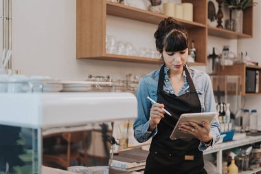 Kahve dükkanı tezgahının arkasında duran bir kahve sahibi. Kafede elinde dijital tabletle ayakta duran bir bayan barista. İş sahibi kavramı.