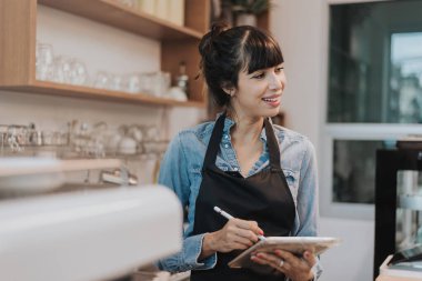 Kahve dükkanı tezgahının arkasında duran bir kahve sahibi. Kafede elinde dijital tabletle ayakta duran bir bayan barista. İş sahibi kavramı.