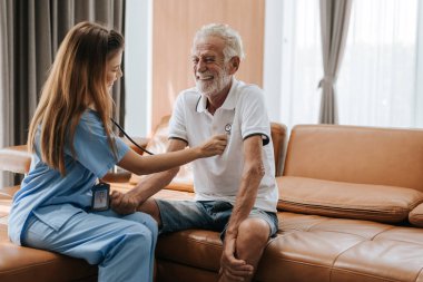 Evde yaşlı bir adamı önemseyen genç hemşire. Asyalı hemşire evdeki yaşlı adama yardım ediyor. Kıdemli sağlık hizmetleri.