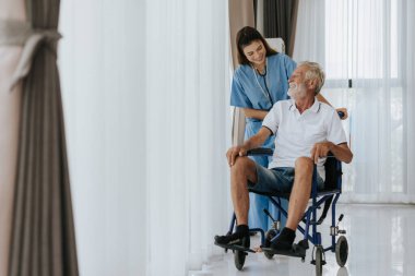 Genç Asyalı hemşire yaşlı adama evde yardım ediyor. Yaşlı bir adam tekerlekli sandalyede oturuyor ve evde genç bir doktorla konuşuyor. Kıdemli sağlık hizmetleri.