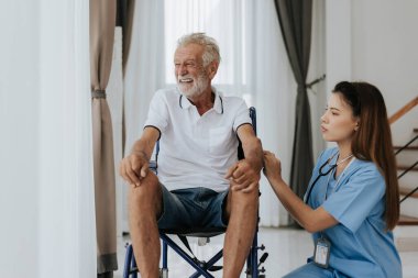 Genç Asyalı hemşire yaşlı adama evde yardım ediyor. Yaşlı bir adam tekerlekli sandalyede oturuyor ve evde genç bir doktorla konuşuyor. Kıdemli sağlık hizmetleri.