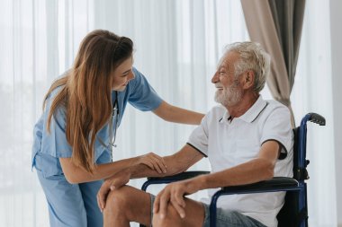 Genç Asyalı hemşire yaşlı adama evde yardım ediyor. Yaşlı bir adam tekerlekli sandalyede oturuyor ve evde genç bir doktorla konuşuyor. Kıdemli sağlık hizmetleri.