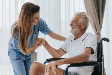 Genç Asyalı hemşire yaşlı adama evde yardım ediyor. Yaşlı bir adam tekerlekli sandalyede oturuyor ve evde genç bir doktorla konuşuyor. Kıdemli sağlık hizmetleri.