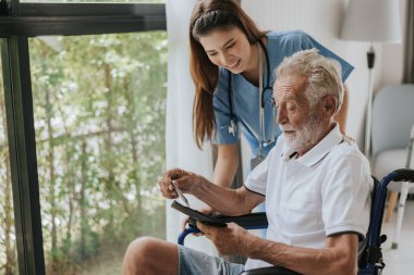 Genç Asyalı hemşire yaşlı adama evde yardım ediyor. Yaşlı bir adam tekerlekli sandalyede oturuyor ve evde genç bir doktorla konuşuyor. Kıdemli sağlık hizmetleri.