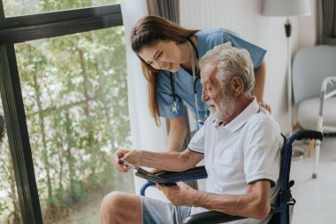 Genç Asyalı hemşire yaşlı adama evde yardım ediyor. Yaşlı bir adam tekerlekli sandalyede oturuyor ve evde genç bir doktorla konuşuyor. Kıdemli sağlık hizmetleri.