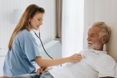 Evde yaşlı bir adamı önemseyen genç hemşire. Asyalı hemşire evdeki yaşlı adama yardım ediyor. Kıdemli sağlık hizmetleri.