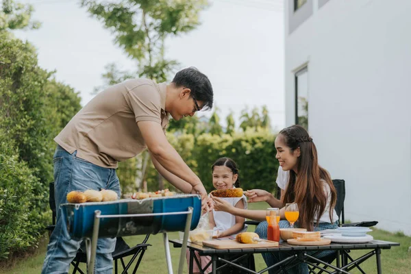 Asian family having dinner in the backyard at home. Happy father doing barbecue with her daughter in houes garden. Barbecue time.