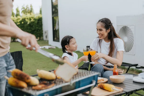 Asian family having dinner in the backyard at home. Happy family with little child camping and have fun in house backyard outside. Barbecue time, Family activities conccept.