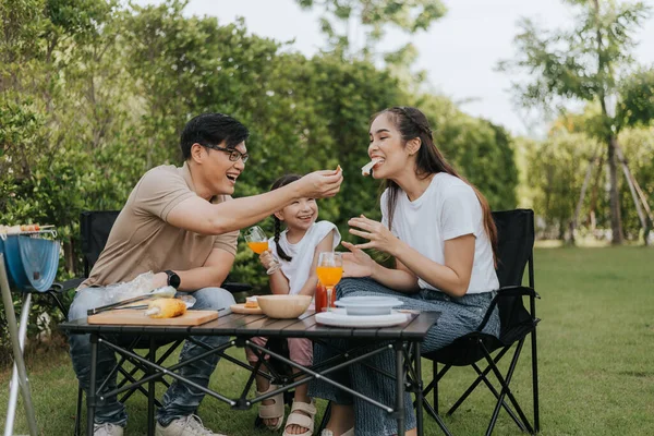 Asian family having dinner in the backyard at home. Happy family with little child camping and have fun in house backyard outside. Barbecue time, Family activities conccept.