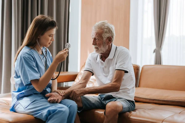 Evde yaşlı bir adamı önemseyen genç hemşire. Asyalı hemşire evdeki yaşlı adama yardım ediyor. Kıdemli sağlık hizmetleri.