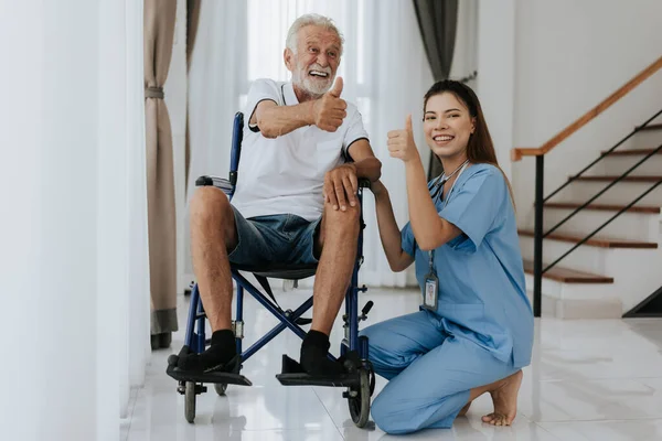 Young asian nurse helping senior man at home. Elderly man sitting on wheelchair and talking with young docter in house. Senior health care.