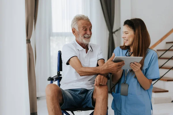 Asian nurse and senior man looking medical record on digital tablet at home. Old man and nurse using digital tablet together to looking health plan. Senior care