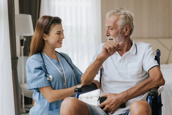 Genç Asyalı hemşire yaşlı adama evde yardım ediyor. Yaşlı bir adam tekerlekli sandalyede oturuyor ve evde genç bir doktorla konuşuyor. Kıdemli sağlık hizmetleri.