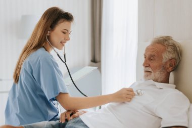 Evde yaşlı bir adamı önemseyen Asyalı hemşire. Genç hemşire yaşlı adama evde yardım ediyor. Kıdemli sağlık hizmetleri.