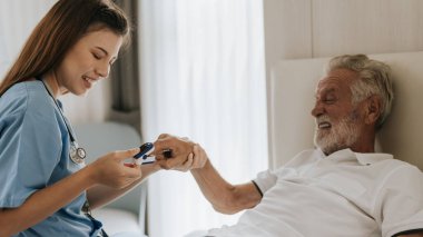 Asyalı hemşire evdeki yaşlı adama oksimetre kullanıyor. Evde kıdemli bir adama yardım eden genç bir hemşire. Kıdemli Sağlık Hizmetleri.