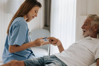 Asyalı hemşire evdeki yaşlı adama oksimetre kullanıyor. Evde kıdemli bir adama yardım eden genç bir hemşire. Kıdemli Sağlık Hizmetleri.