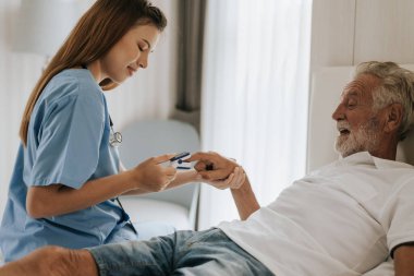 Asyalı hemşire evdeki yaşlı adama oksimetre kullanıyor. Evde kıdemli bir adama yardım eden genç bir hemşire. Kıdemli Sağlık Hizmetleri.