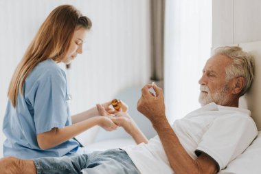 Hemşire kıdemli adama uyuşturucu veriyor. Genç Asyalı hemşire evde yaşlı bir adama bakıyor. Kıdemli sağlık hizmetleri.