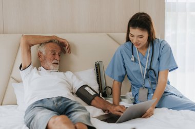 Asyalı hemşire evde yaşlı bir adamın tansiyonunu ölçüyor. Genç hemşire yaşlı adama evde yardım ediyor. Kıdemli sağlık hizmetleri.