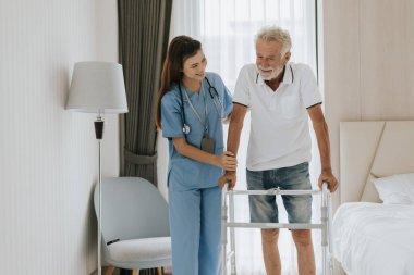 Asyalı hemşire kıdemli adamın evde dolaşmasına yardım ediyor. Genç hemşire yaşlı adama evde yardım ediyor. Kıdemli sağlık hizmetleri.
