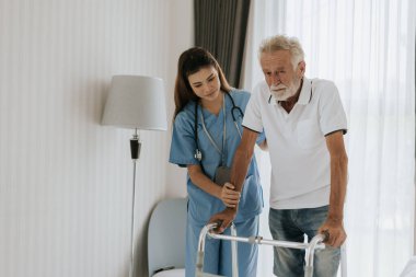 Asyalı hemşire kıdemli adamın evde dolaşmasına yardım ediyor. Genç hemşire yaşlı adama evde yardım ediyor. Kıdemli sağlık hizmetleri.