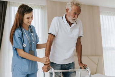 Asyalı hemşire kıdemli adamın evde dolaşmasına yardım ediyor. Genç hemşire yaşlı adama evde yardım ediyor. Kıdemli sağlık hizmetleri.