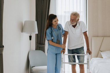 Asyalı hemşire kıdemli adamın evde dolaşmasına yardım ediyor. Genç hemşire yaşlı adama evde yardım ediyor. Kıdemli sağlık hizmetleri.