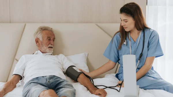 Asian nurse measuring blood pressure of elderly man at home. Young nurse helping senior man at home. Senior health care.