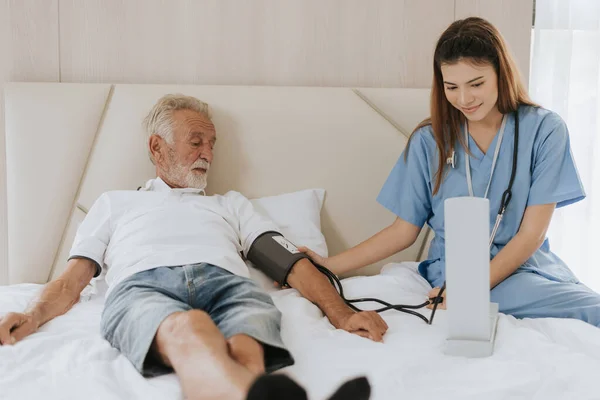 Asian nurse measuring blood pressure of elderly man at home. Young nurse helping senior man at home. Senior health care.