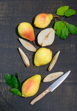 Kırmızı ve sarı armutlar koyu ahşap arka planda yatar. Arka planda bir bıçak ve yeşil yapraklar var. Üst görünüm