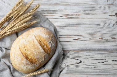 Açık peçetede çıtır çıtır bir kabukla taze ekmek. Açık ahşap bir masada buğday kulakları. Üst görünüm, metin için boşluk