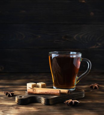 Koyu kahverengi bir tahtanın üzerinde şeffaf bir fincanda tarçın kokulu sıcak çay.