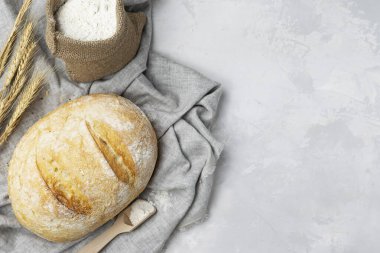 Betonun altındaki ışıklı masada taze kabuklu ekmek. Buğday kulakları ve un hafif bir peçetenin üzerinde bir bez torba içinde. Üst görünüm, metin için boşluk