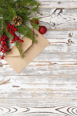 Hafif ahşap bir zemin üzerinde kraft kağıdından yapılmış bir zarf. Üst Manzara. Mesaj için yer var. Sol üst köşesinde kırmızı böğürtlen bulunan ladin dalları. Noel ve Yeni Yıl tebrik kartı